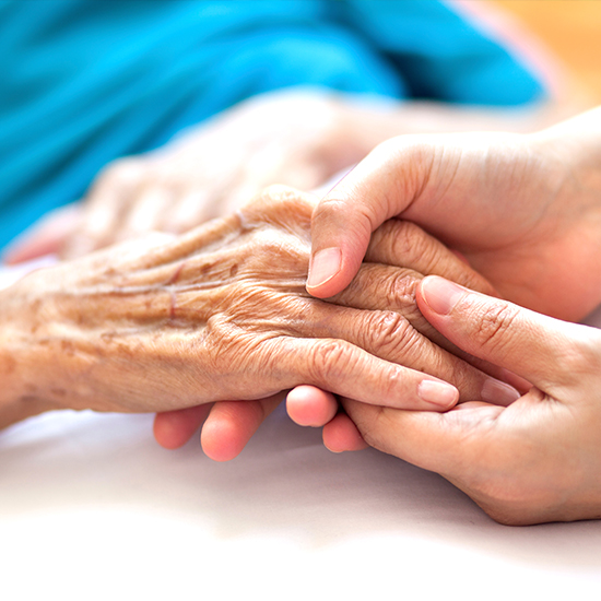 photo of a caregiver's hand is holding a senior's hand gently.